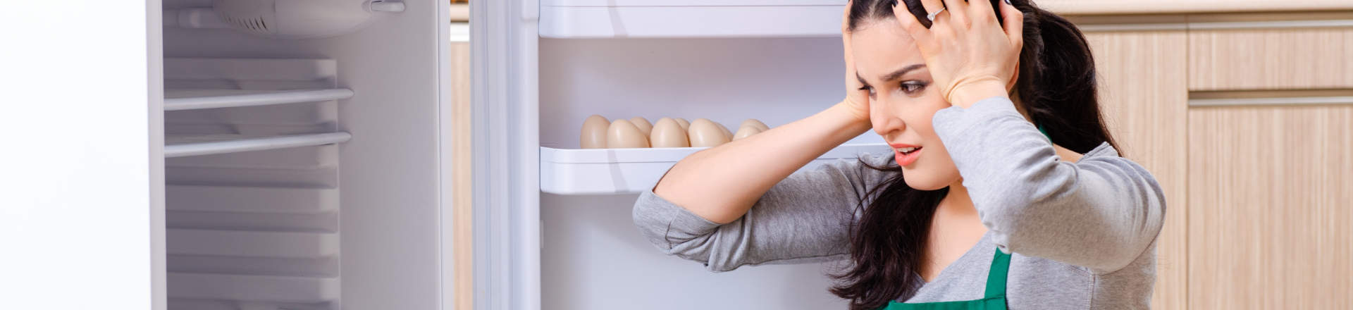 shocked woman clutching her head in front of open fridge